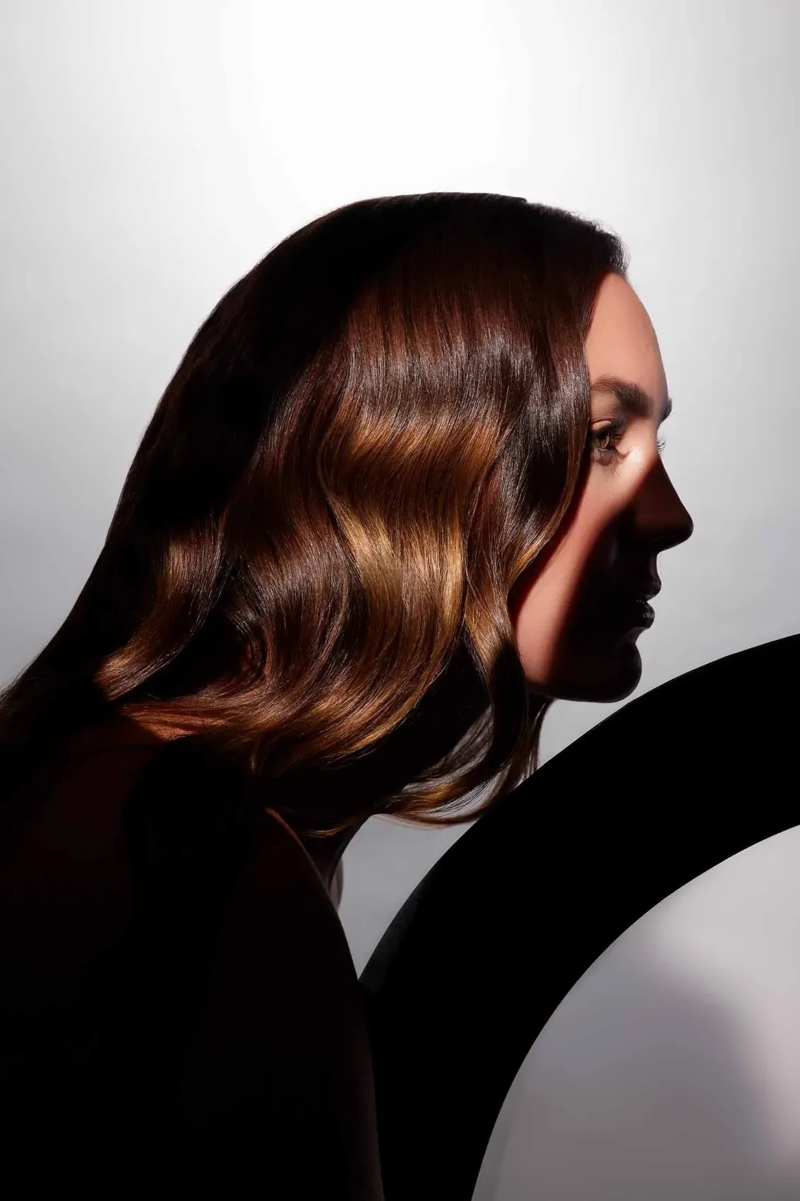 Model in profile with glossy brunette waves against a white curve