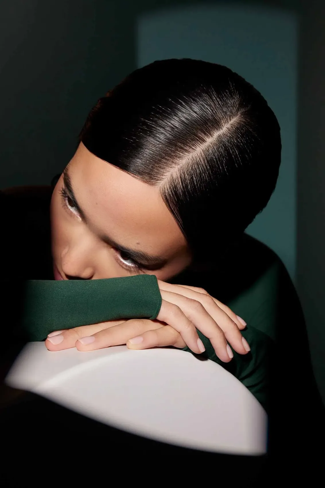 Model with sleek center-parted dark hair resting on a curved white form