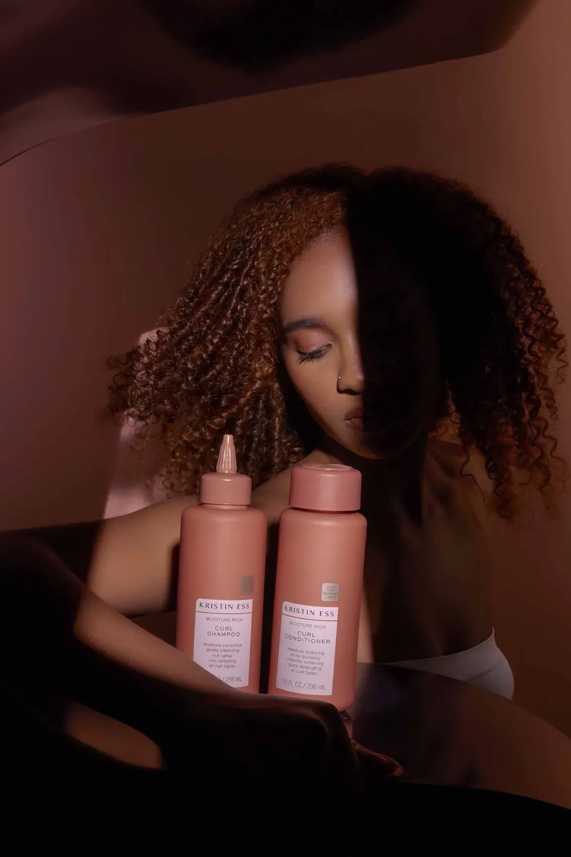 Model with curly hair holding two pink Kristin Ess bottles