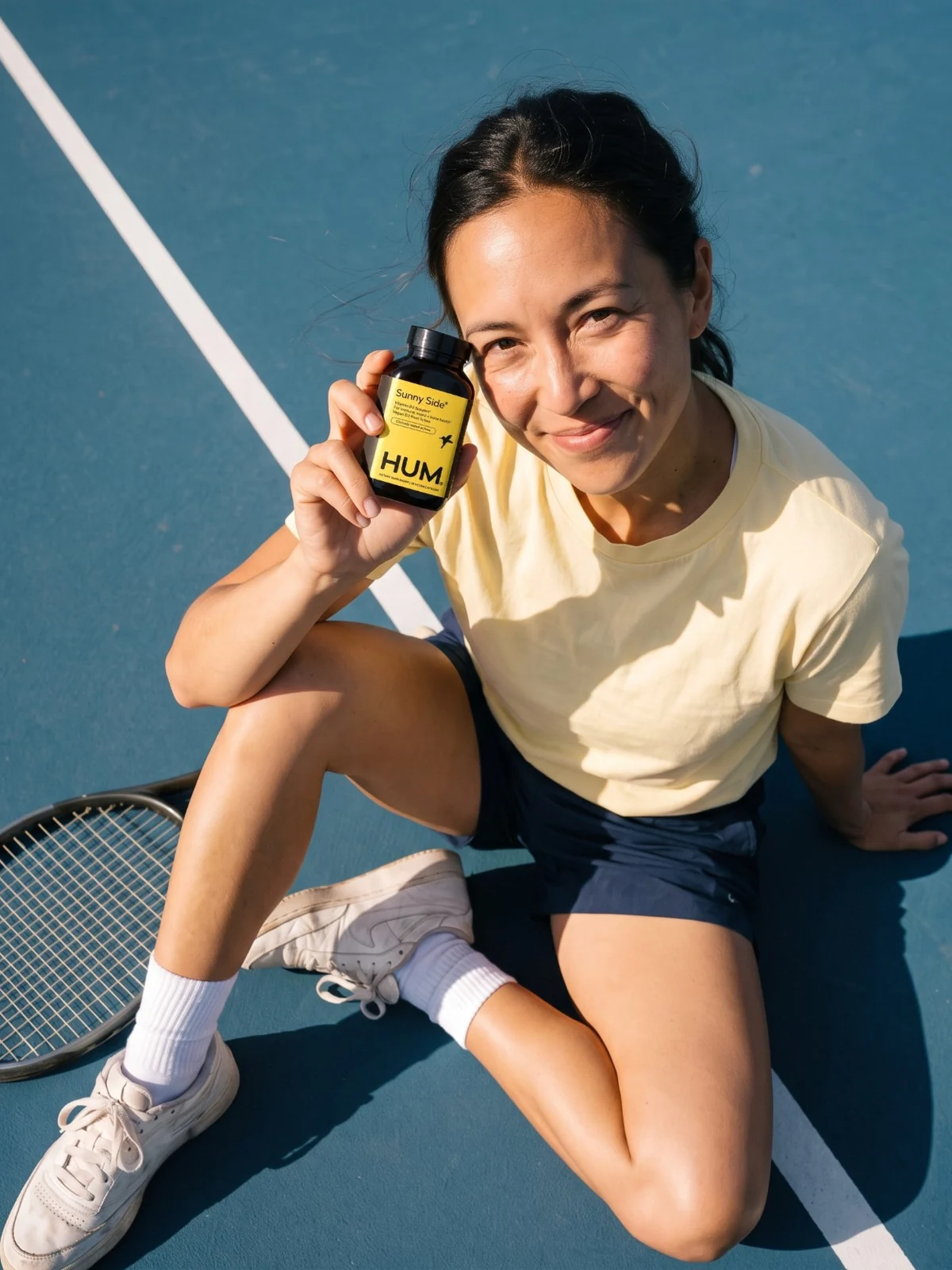 Woman sitting on a blue tennis court holding up a Sunny Side bottle