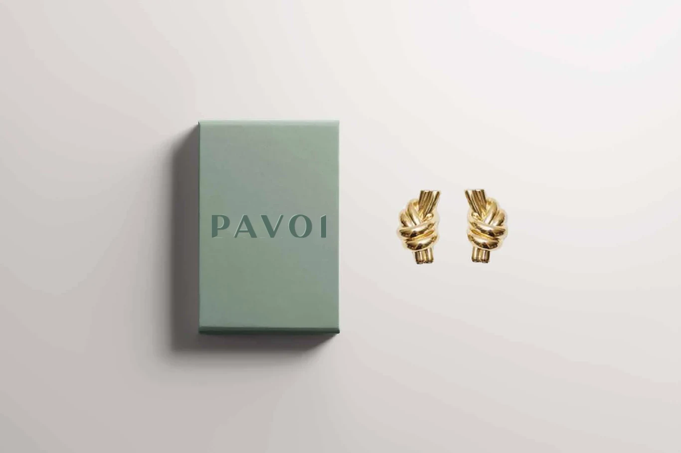 Sage PAVOI jewelry box with a debossed wordmark beside gold earrings