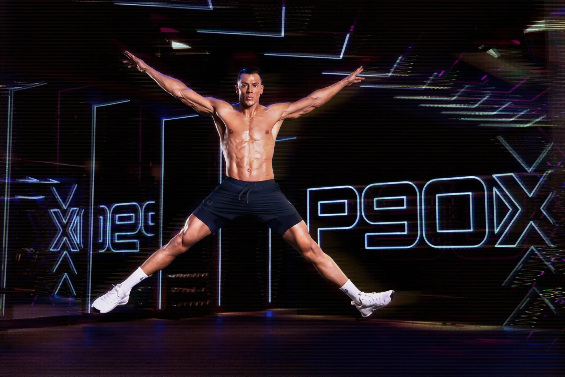P90X trainer mid star jump in front of the glowing neon P90X wordmark